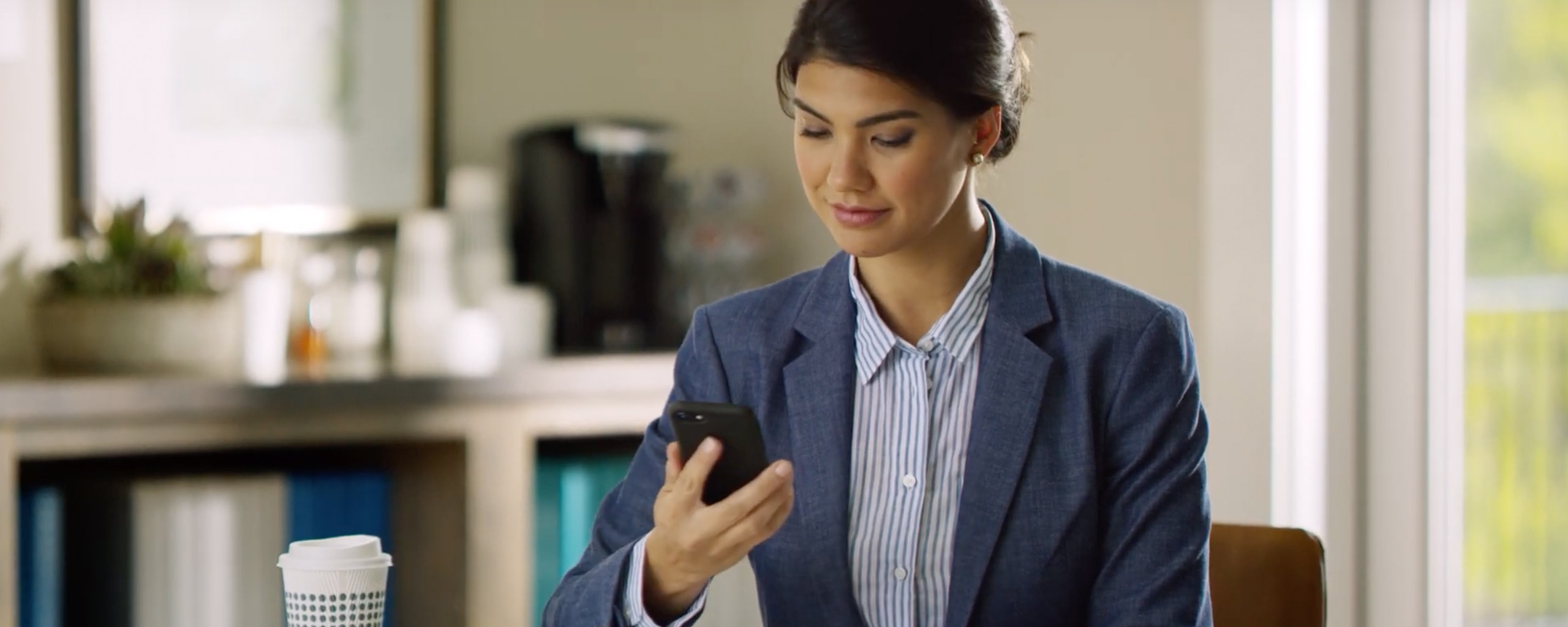 Woman in blue blazer looking down at a black cell phone in her hands