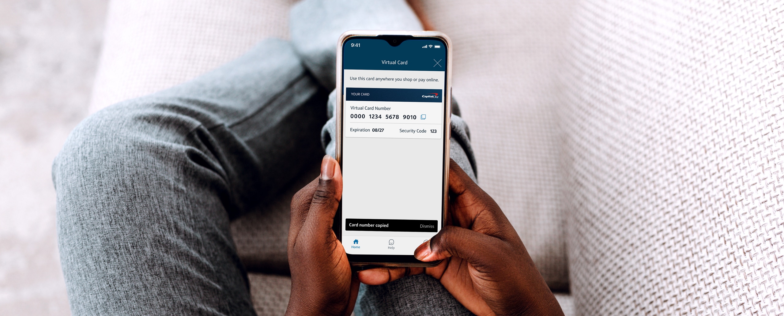 Person sitting on couch holding their mobile device with a virtual card number on screen.