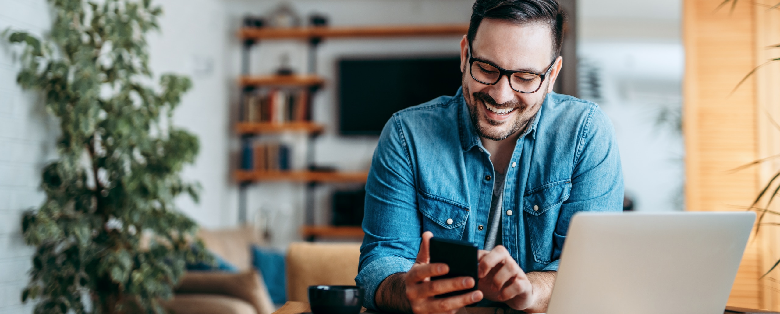 Person with laptop looking at a mobile phone.