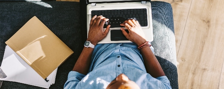 Person typing on a laptop with documents and folder nearby, planning wedding budget.