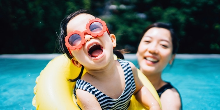 Smiling woman and happy child play in a pool on a hot summer day.