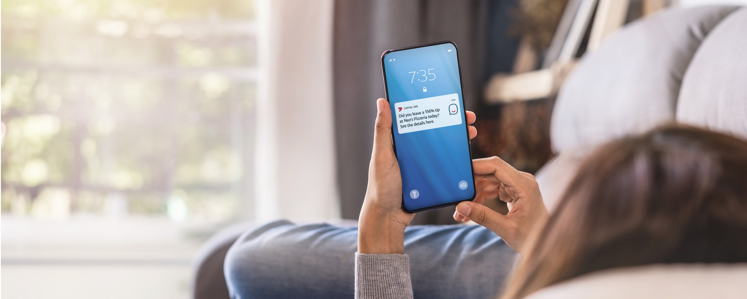 Person holding a smartphone has a notification from Eno, Capital One’s virtual assistant.