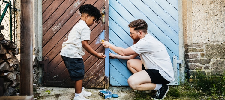 Father and son painting an old wooden gate