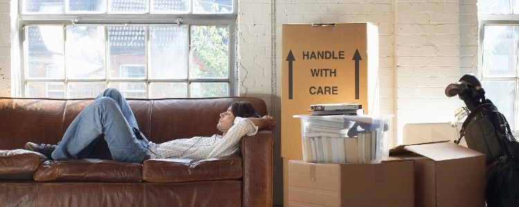 Person resting on a couch near moving boxes after paying rent for a new apartment.