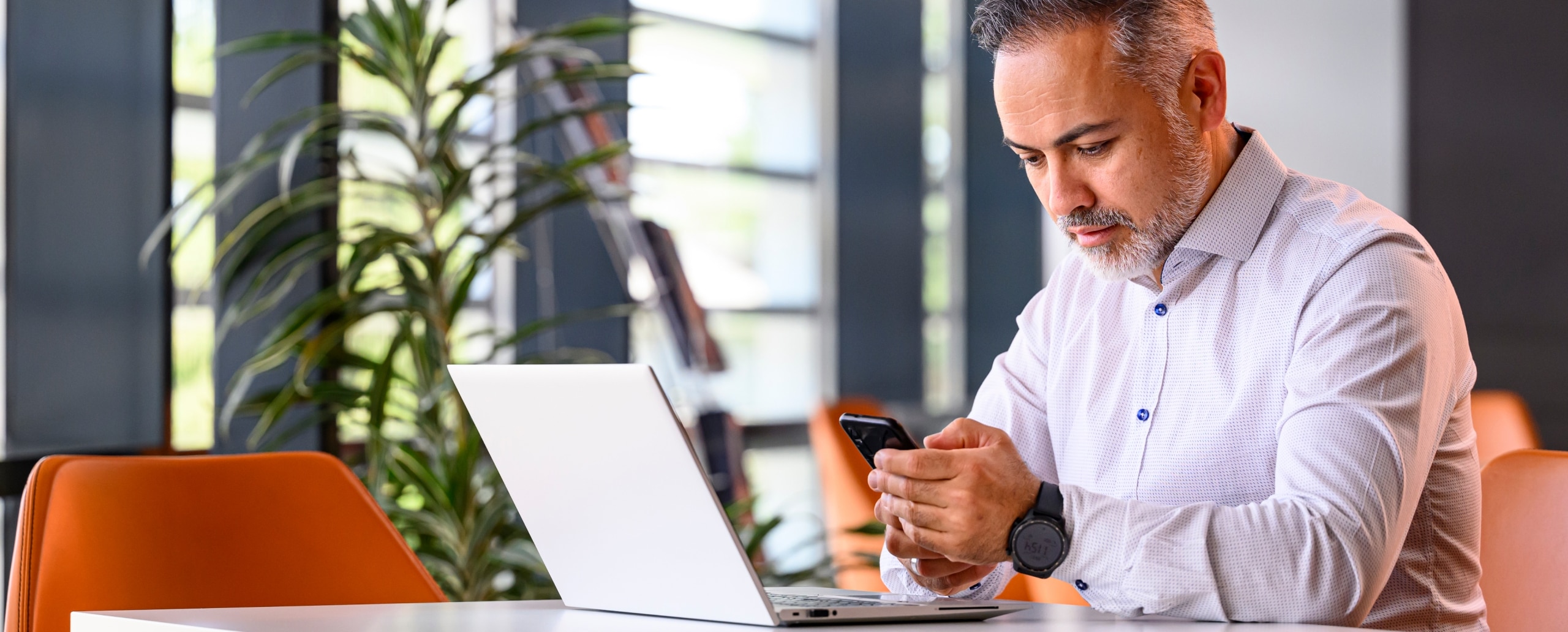 Person with laptop looking at a mobile phone.