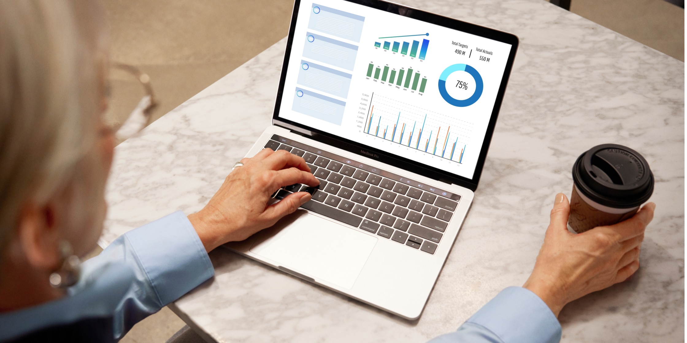 A person works on a laptop with the accounting tool QuickBooks open on the screen. They have a cup of coffee in their right hand while their left hand is typing on the laptop keys.