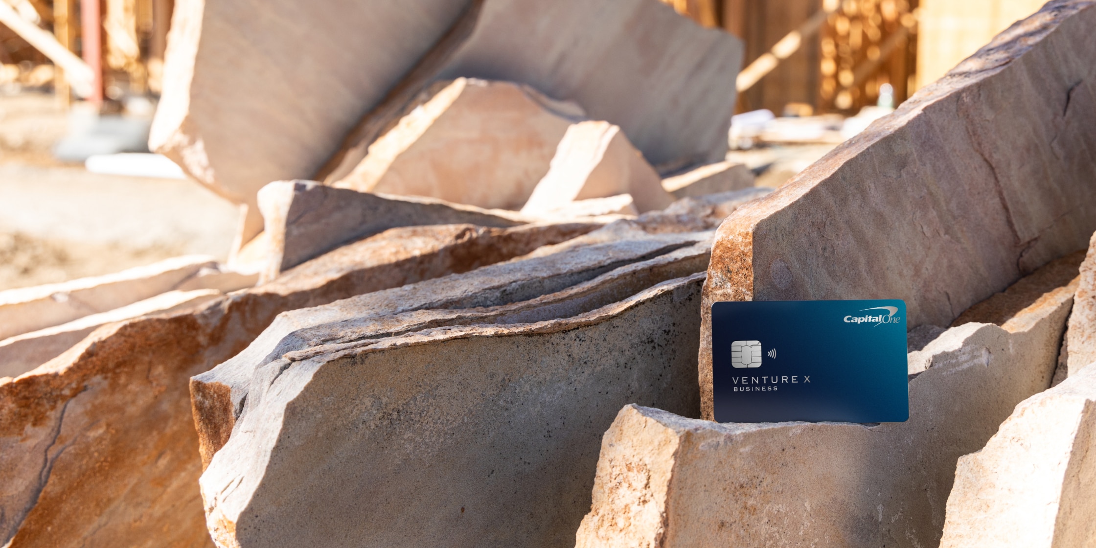A blue Capital One Venture X Business card sits on stones.