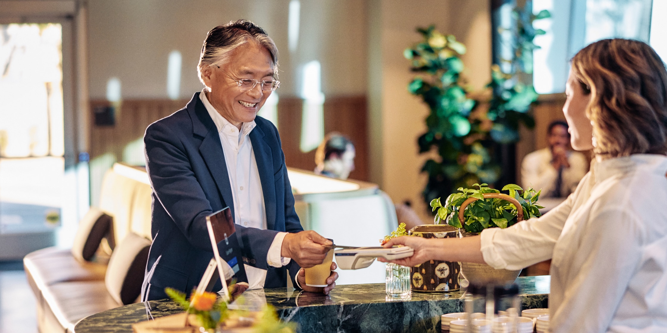 A person in a business suit pays for a takeout cup of coffee by tapping his credit card against a portal.