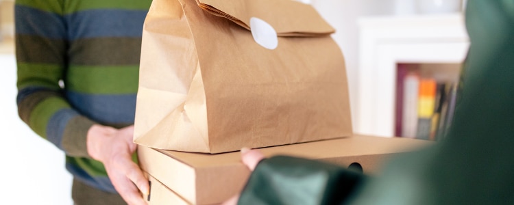 Delivery person hands bags of food to a customer through the doorway.