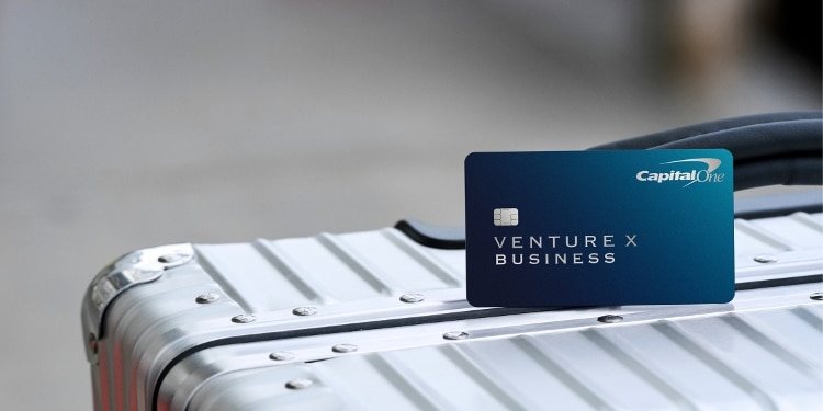 The blue Capital One Business Venture X Business card rests on top of a silver luggage.