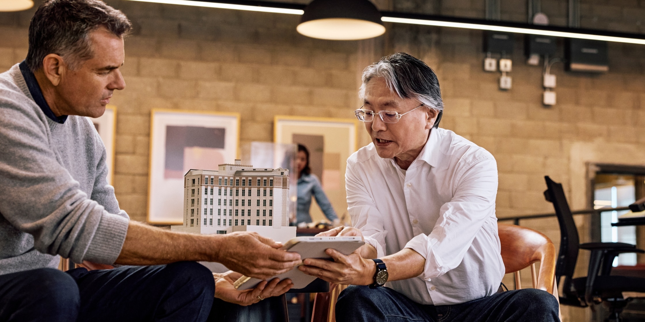 Two men in an office look together at something on a digital tablet. Each is holding one side of the tablet.