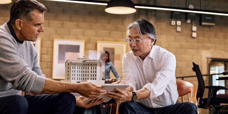 Two men in an office look together at something on a digital tablet. Each is holding one side of the tablet.