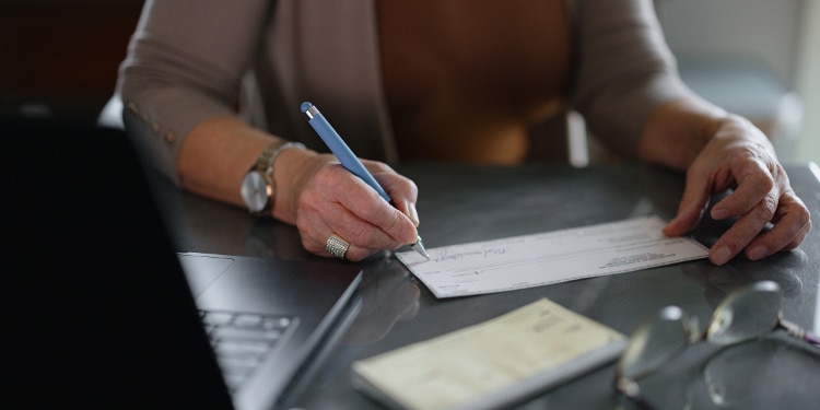 A close-up shot of a woman’s hand writing a check.