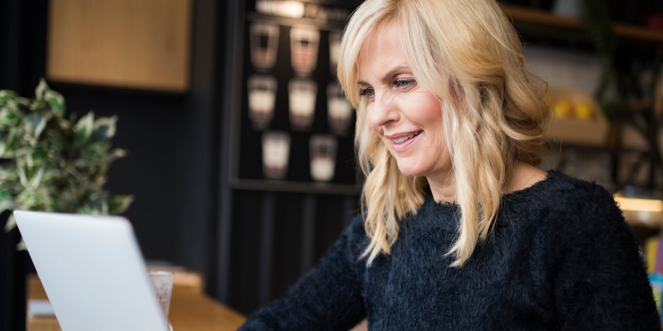 A woman in a dark sweater sits at a desk working on a laptop.