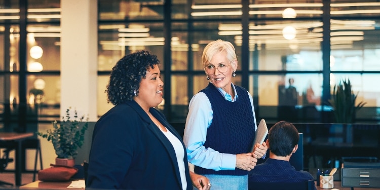 Two women walk through an office together.