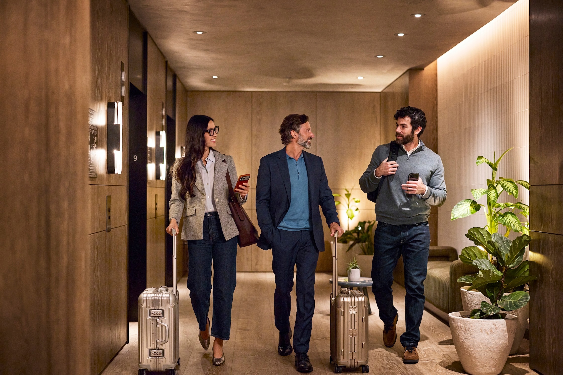 Group of business travelers chatting while walking through a hotel lobby with their luggage.