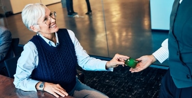 Business owner handing her Capital One Spark Cash Plus card to another individual while smiling.