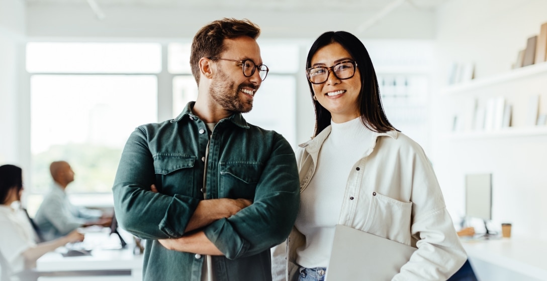 Two business owners standing in their workspace while smiling.