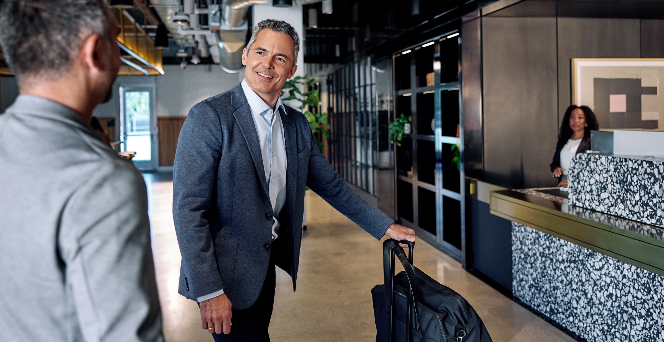 A business owner waiting in the lobby of a hotel with their suitcase.