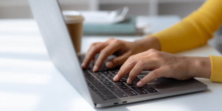 A person wearing a yellow sweater typing on a laptop at a desk.