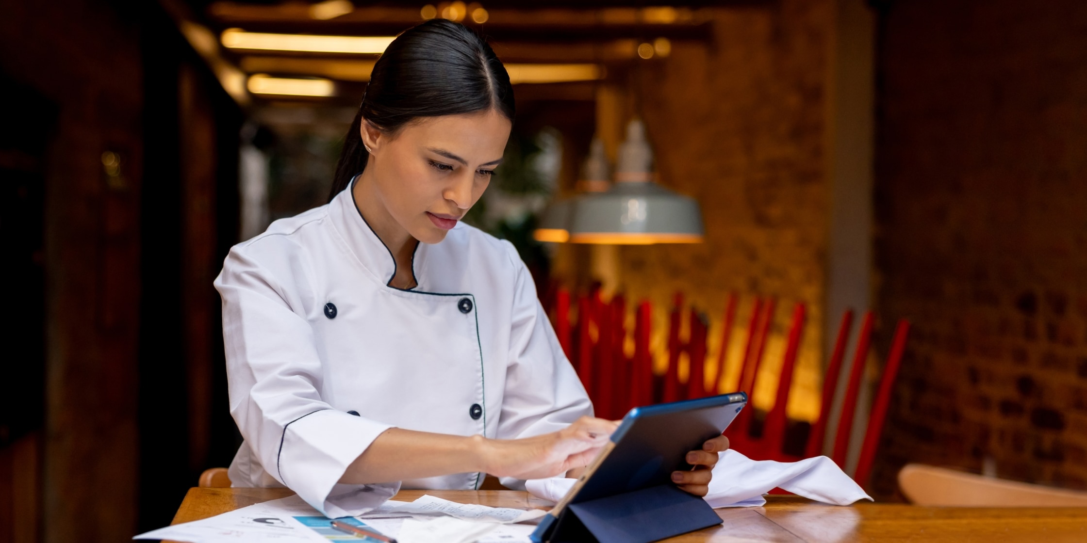 A female chef doing the books at a restaurant, representing a business owner managing rising costs with cash back.