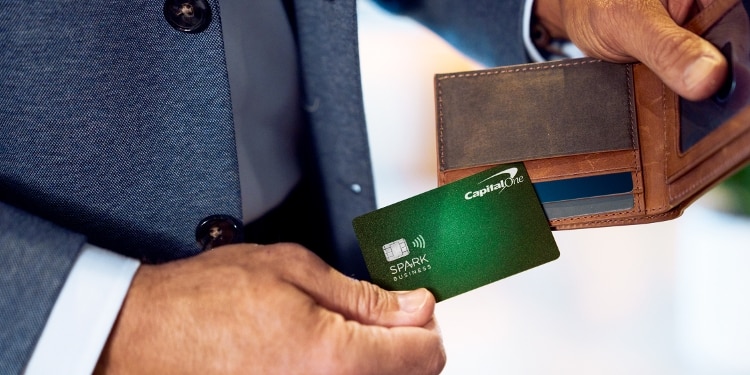 A close-up of a person pulling his green Capital One Spark business card out of his wallet. His wallet has other credit cards in it as well.
