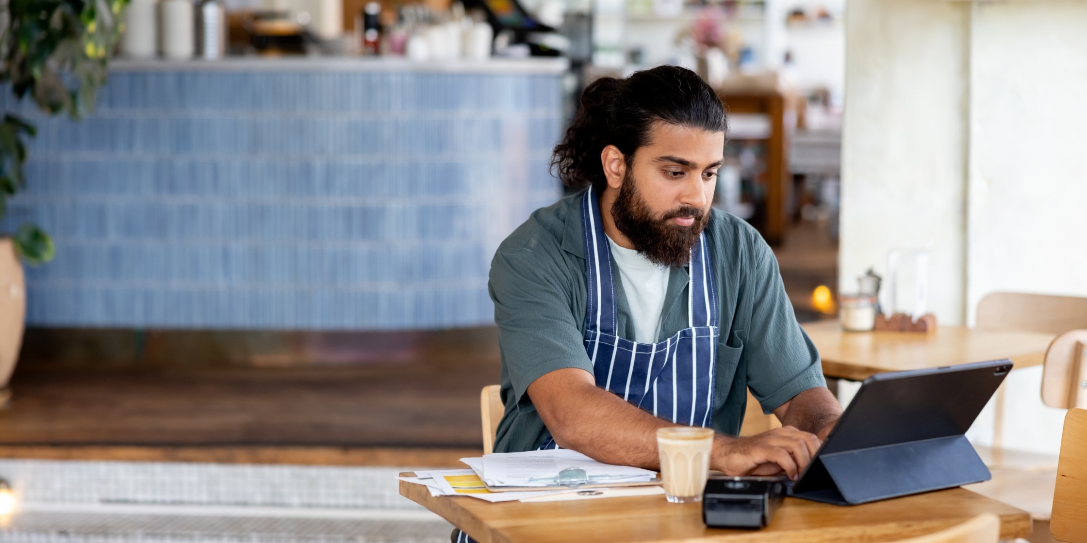 A cafe manager doing accountancy on a digital device, securely managing payments to prevent accounts payable fraud.