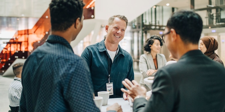 Colleagues talk together while standing around a table in an office.