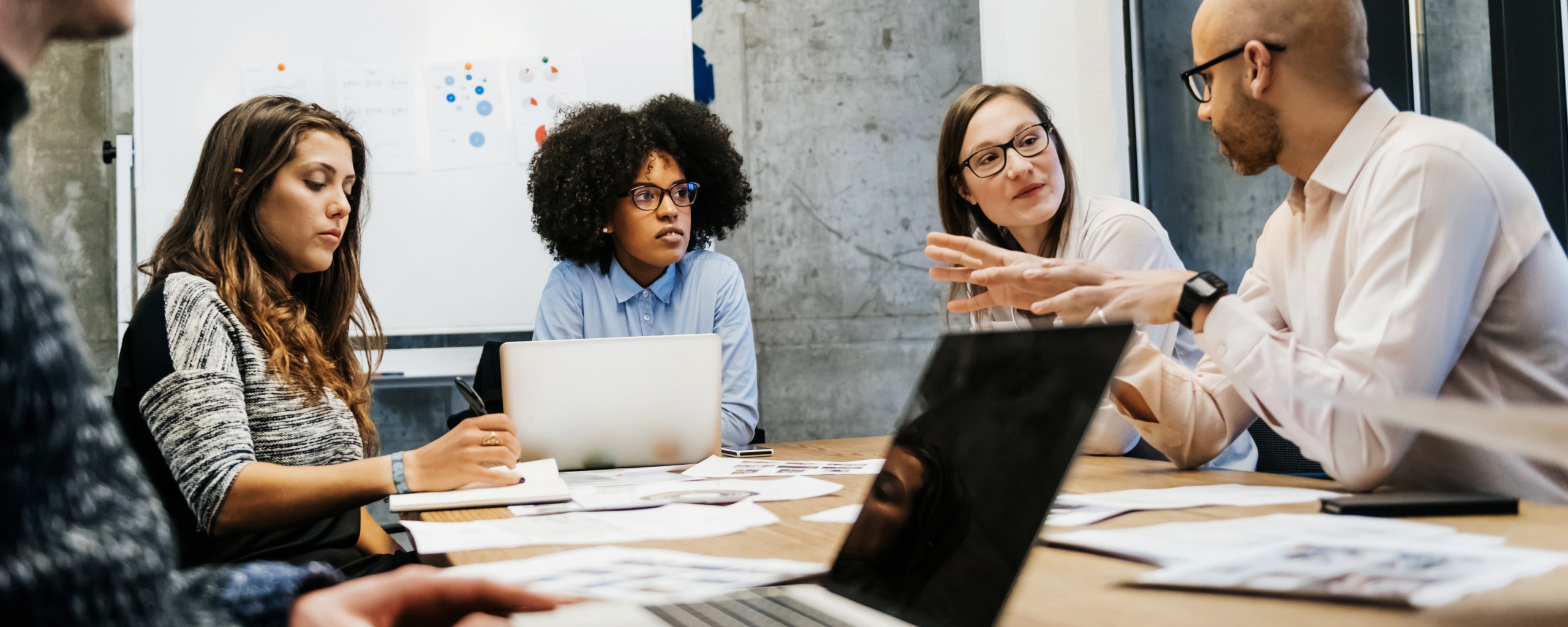 Three women leading a business meeting with a group around a conference table.