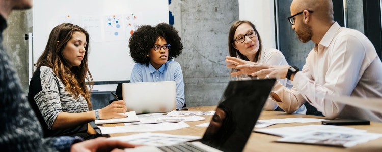 Three women leading a business meeting with a group around a conference table.