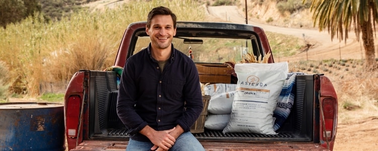 Jorge Gaviria, owner of Masienda, sits in the back of a red pickup truck on a farm with bags of his company's masa beside him.