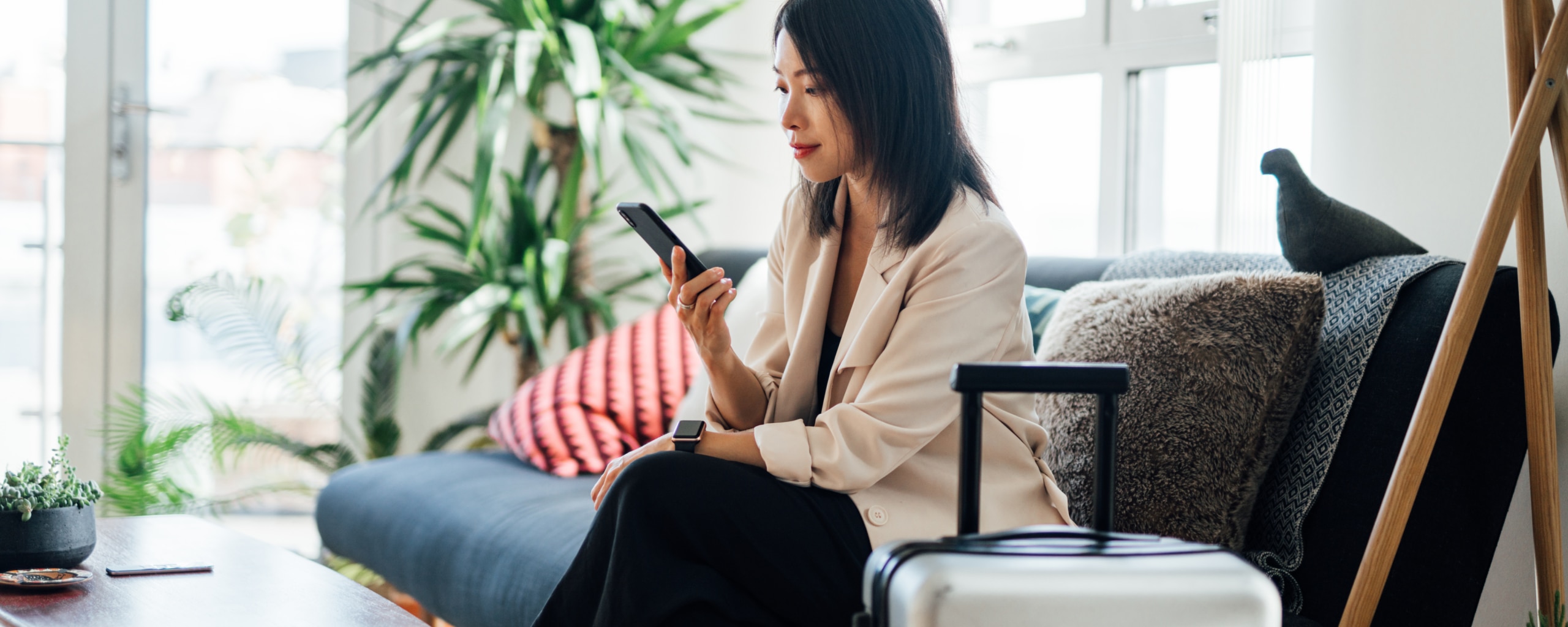 Woman sitting on couch with luggage looking at mobile phone.