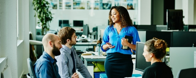 A leader speaking to three employees in a workplace setting.