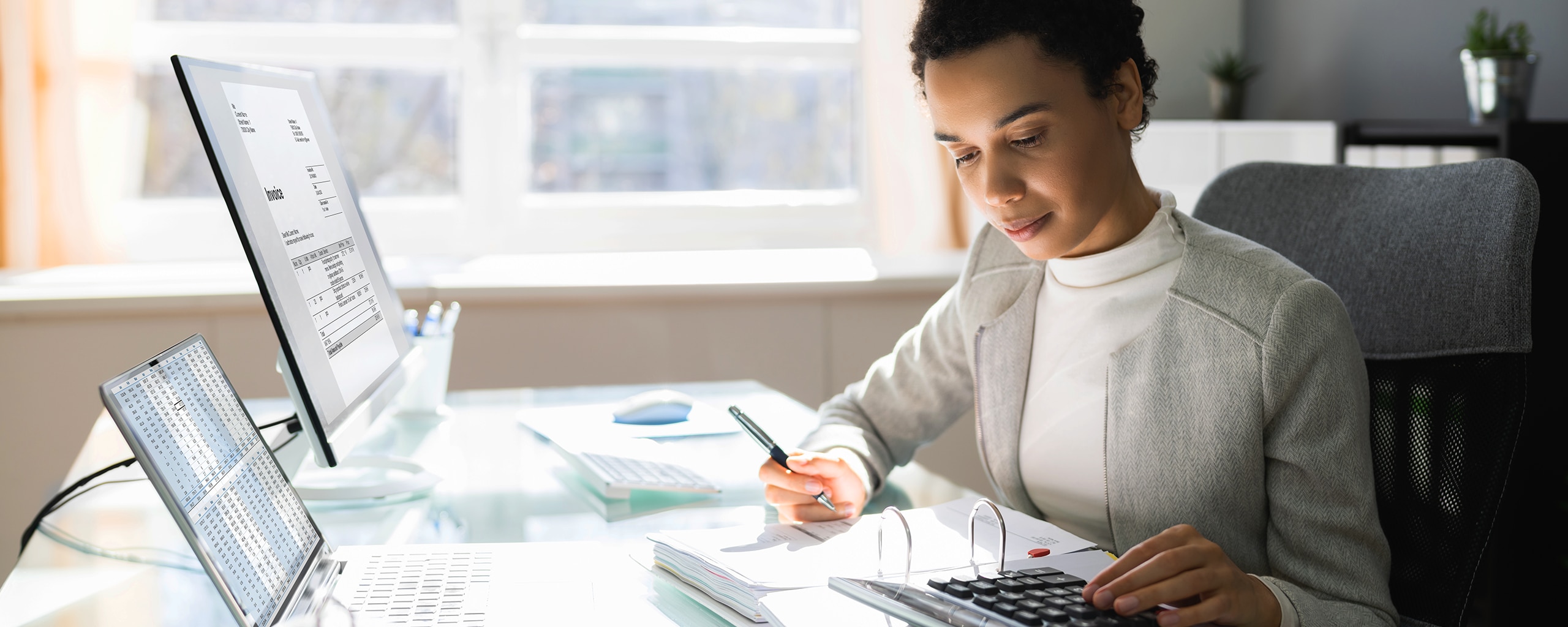 Woman sitting at a desk working on calculations using a laptop and calculator.
