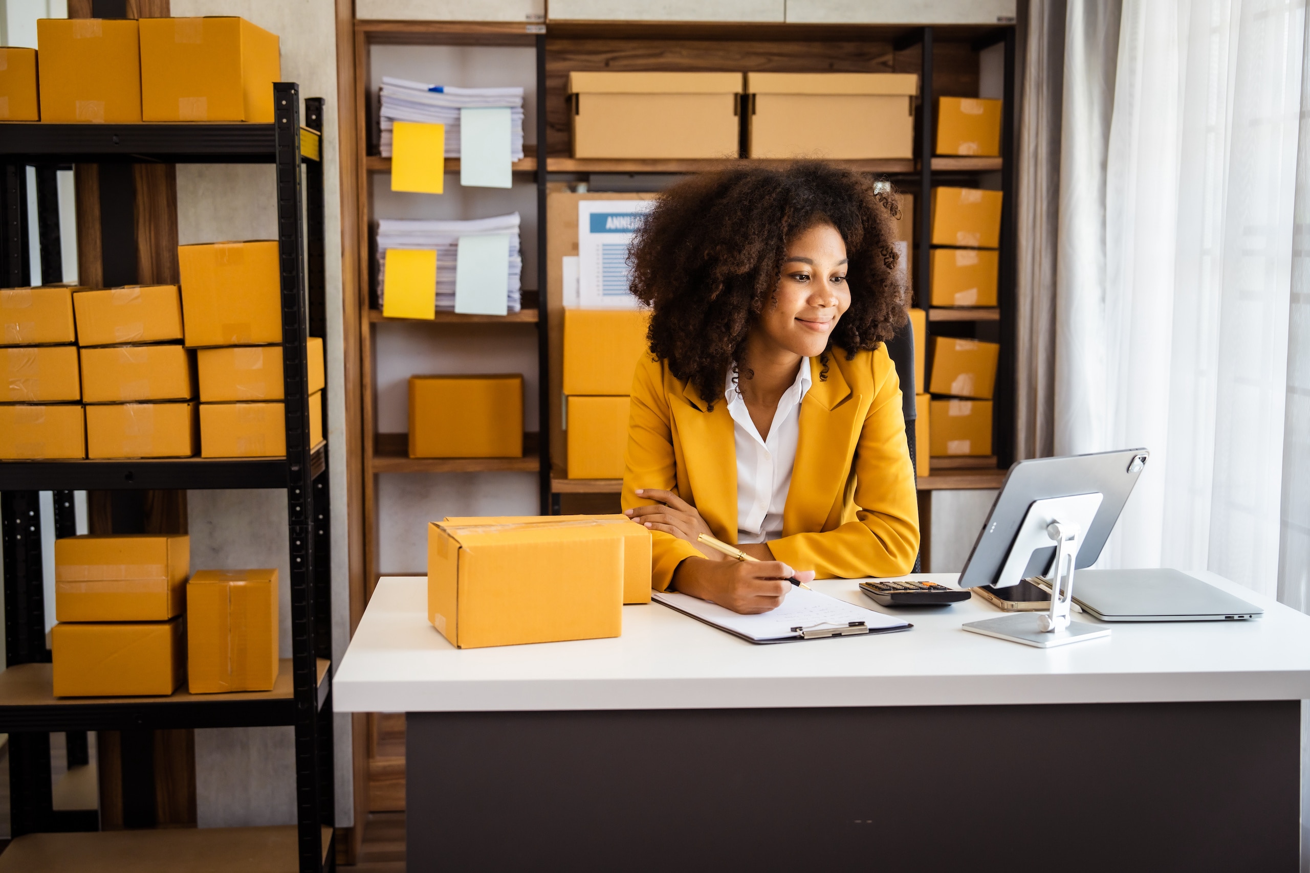Women sitting at desk working at a computer in a room with shelves of shipping boxes.