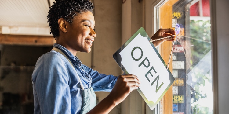 A woman flips a store sign from “closed” to “open.”