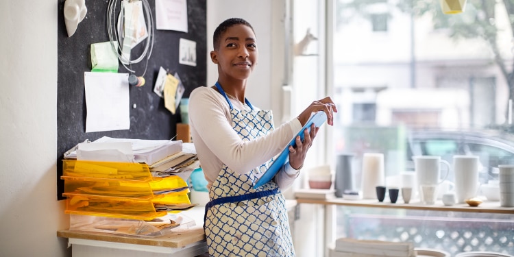 A woman wearing an apron and holding a clipboard stands in a shop next to file organizers.