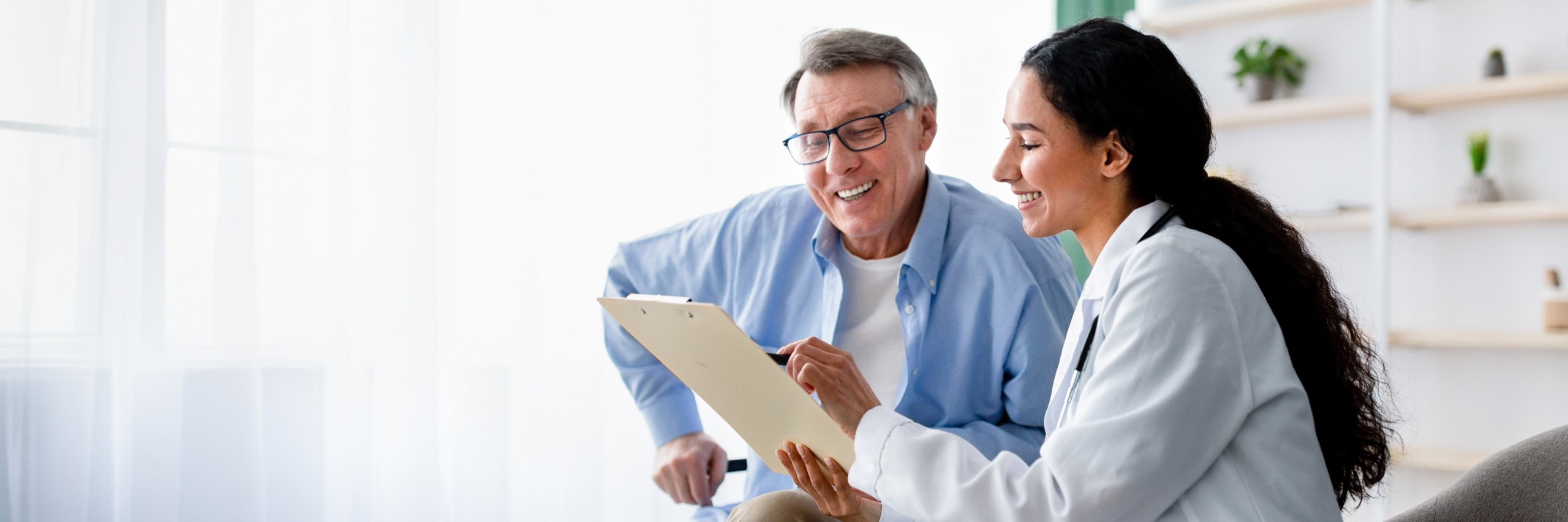 Female doctor looks over chart with male patient in a clinical setting.