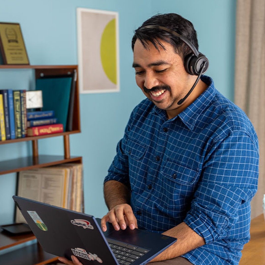 Man sits in home office wearing headset and smiling at his laptop