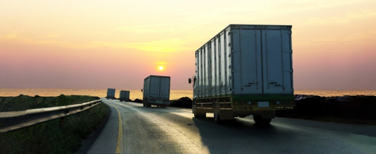 2 trucks driving down highway towards sunset