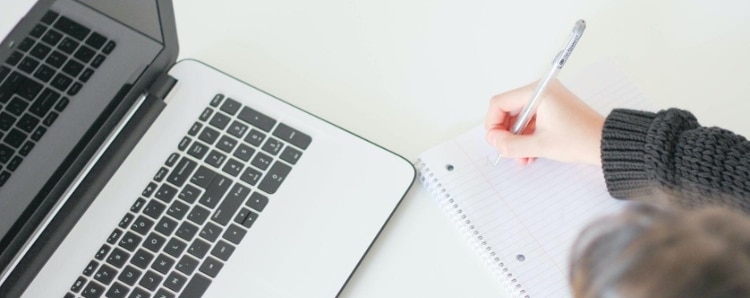 closeup shot of someone taking notes on a notepad, next to an open laptop