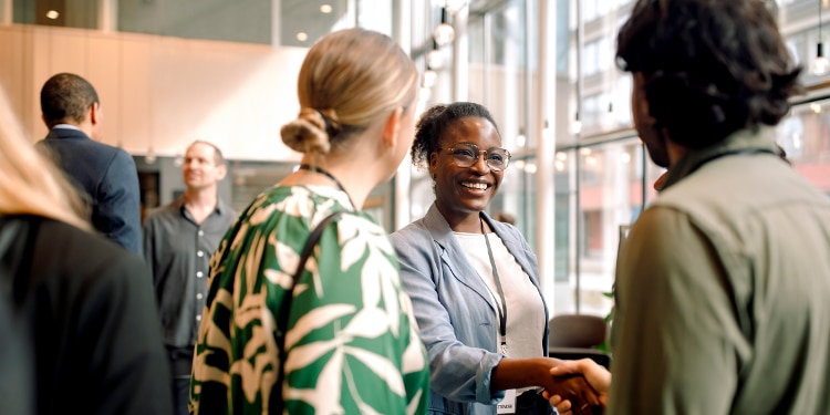 Woman smiling shaking hands with man within group at a conference.