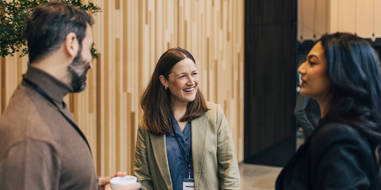 Smiling woman converses with man and woman at conference