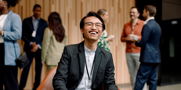 Man smiling at academic conference as other attendees mingle in background