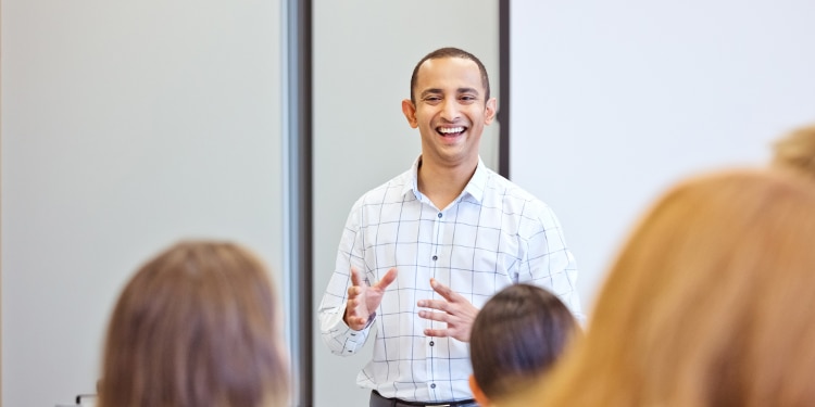 Smiling man speaks to individuals in a classroom setting