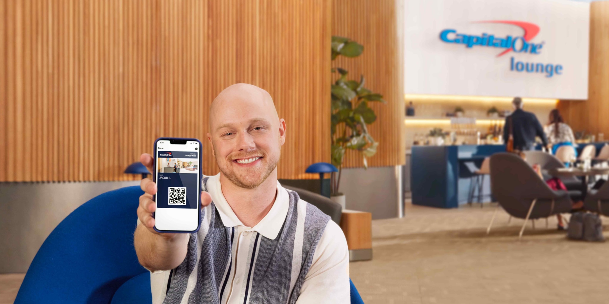 Capital One associate sitting in Capital One Lounge showing digital wallet on smart phone.