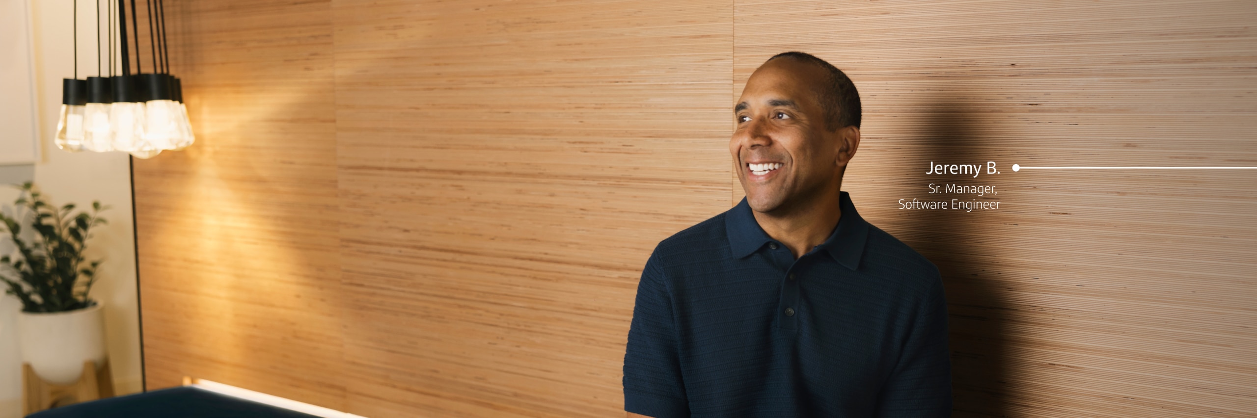 Jeremy B., Software Engineer, stands smiling against wood wall