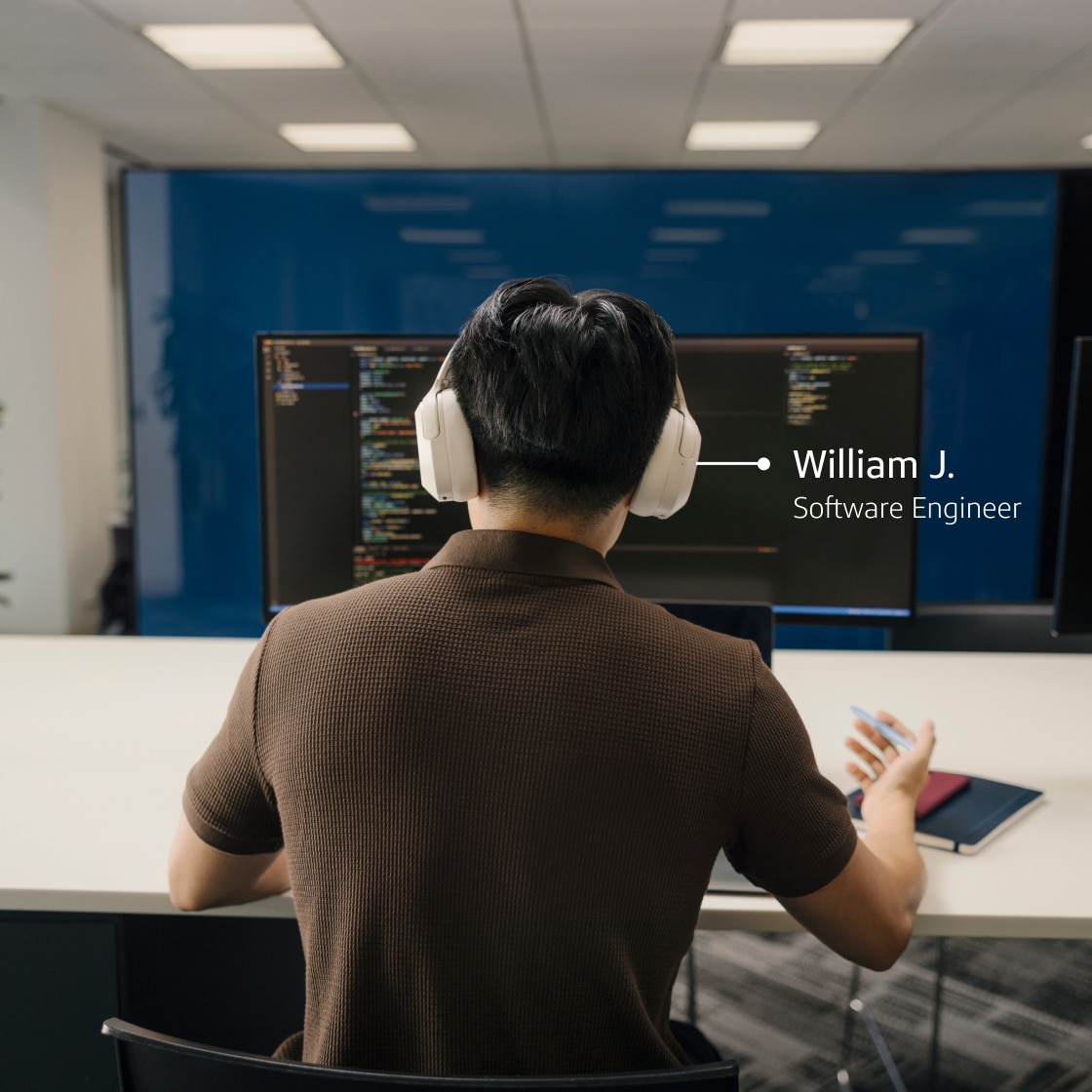 William J., Software Engineer, works at desk wearing headphones and looking at code on monitor