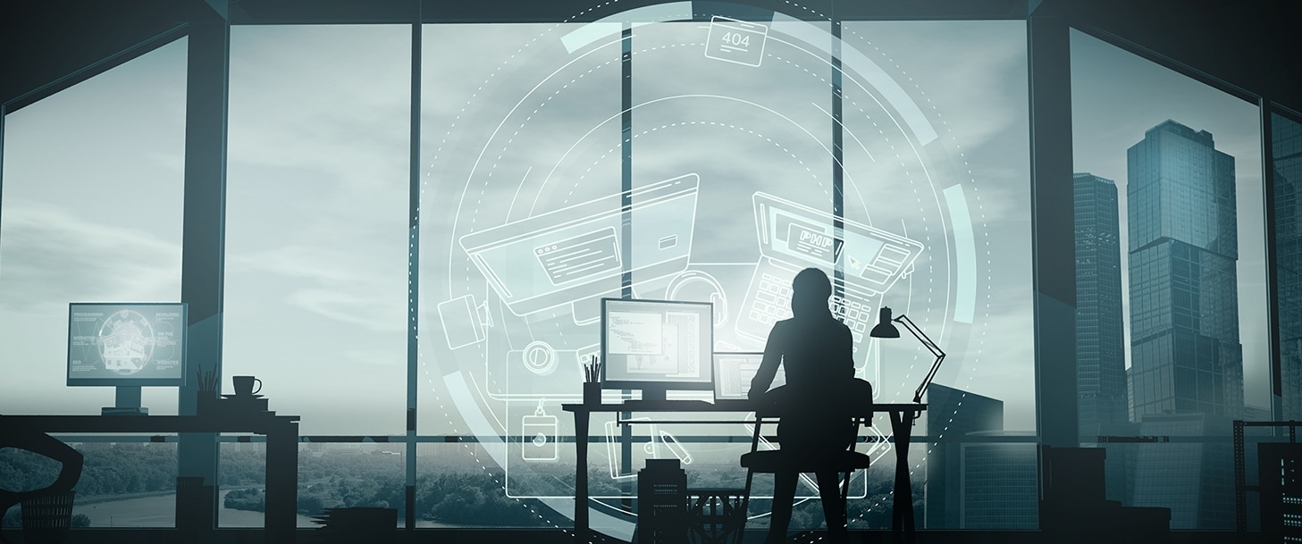 woman sitting at desk with computer, facing window that is overlooking city skyline