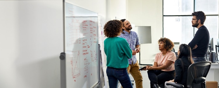 Group of young professionals surrounding a whiteboard where they are making notes.